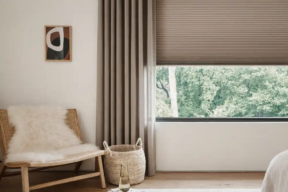 Bej plise perdeli, ahşap sandalyeli ve doğal ışık alan sıcak ve sade iç mekân köşesi.