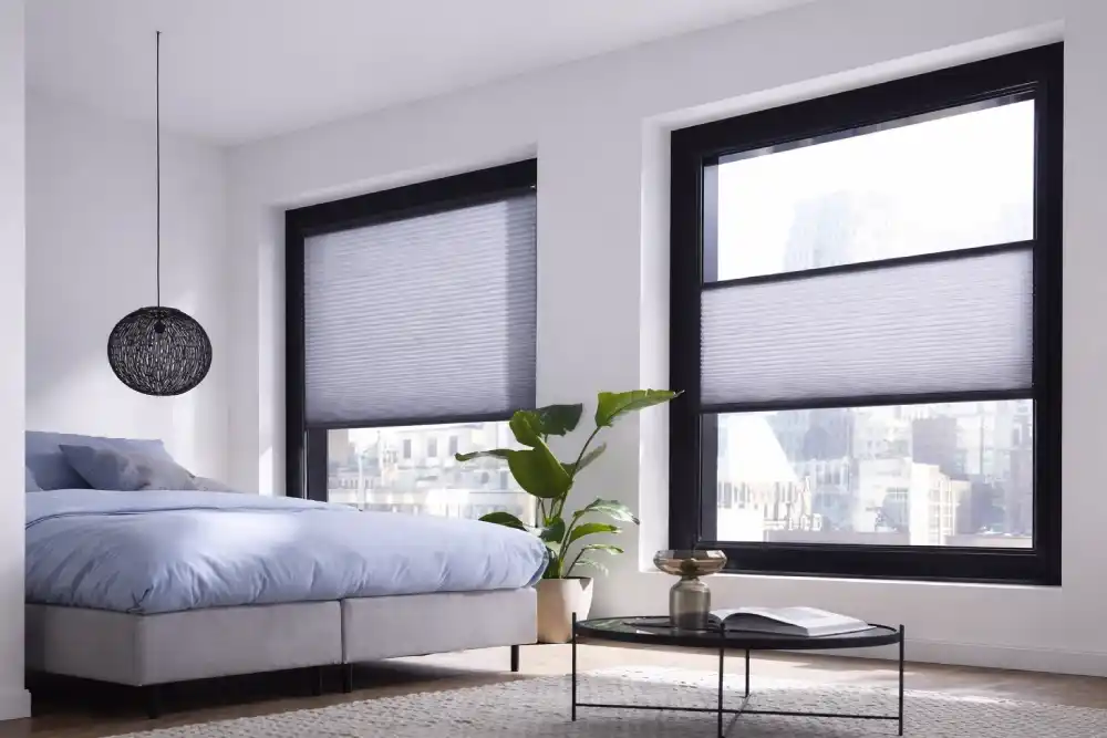 Büyük siyah çerçeveli pencerelere ve gri plise perdelere sahip modern yatak odası iç mekânı